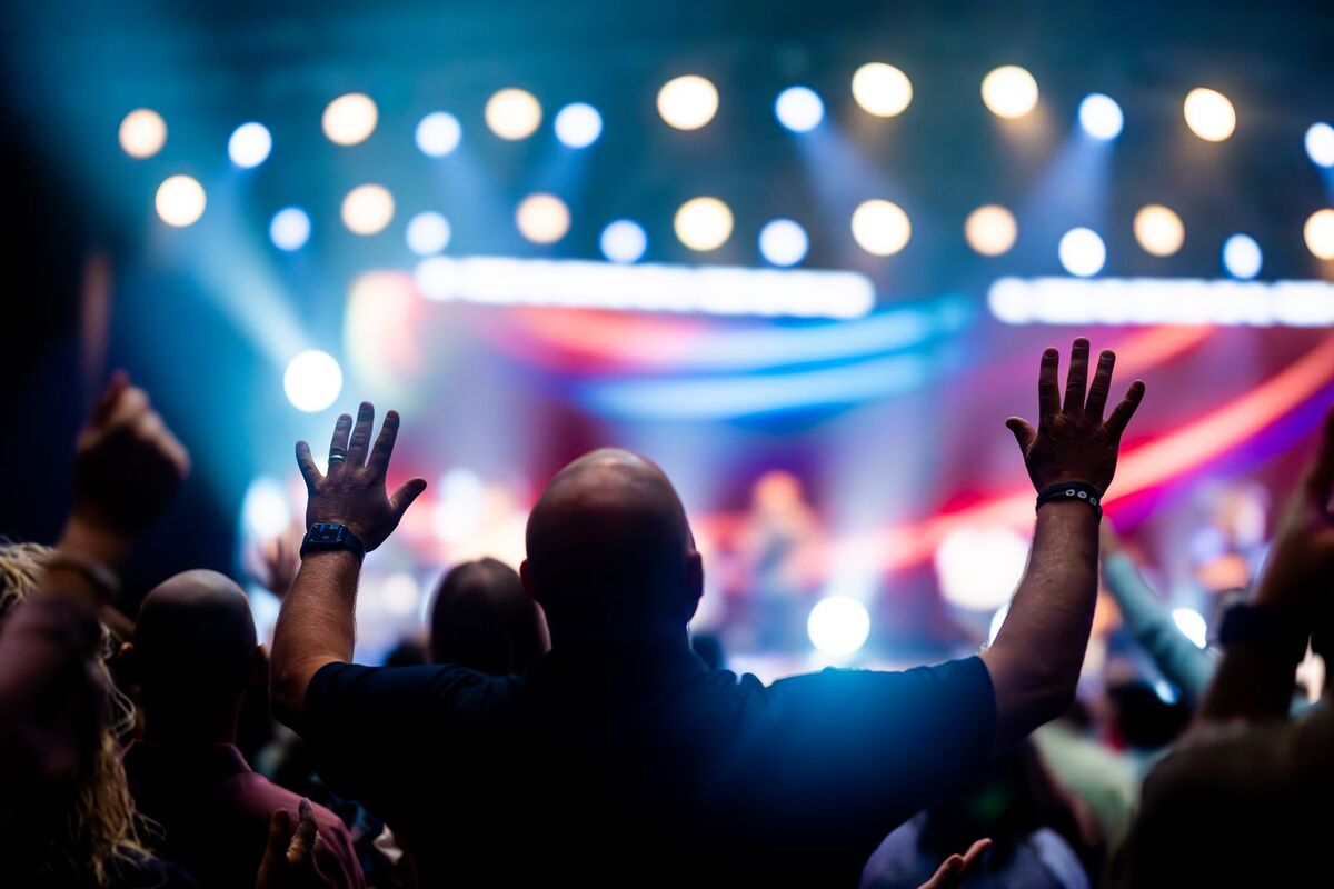 Crowd with hands raised in front of a lit concert stage
