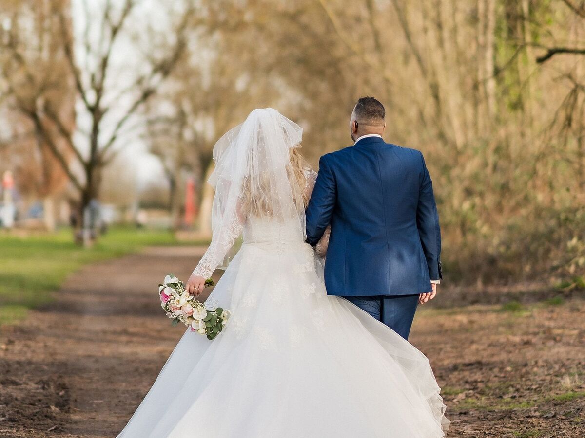 Bride and groom walking together down a tree-lined path